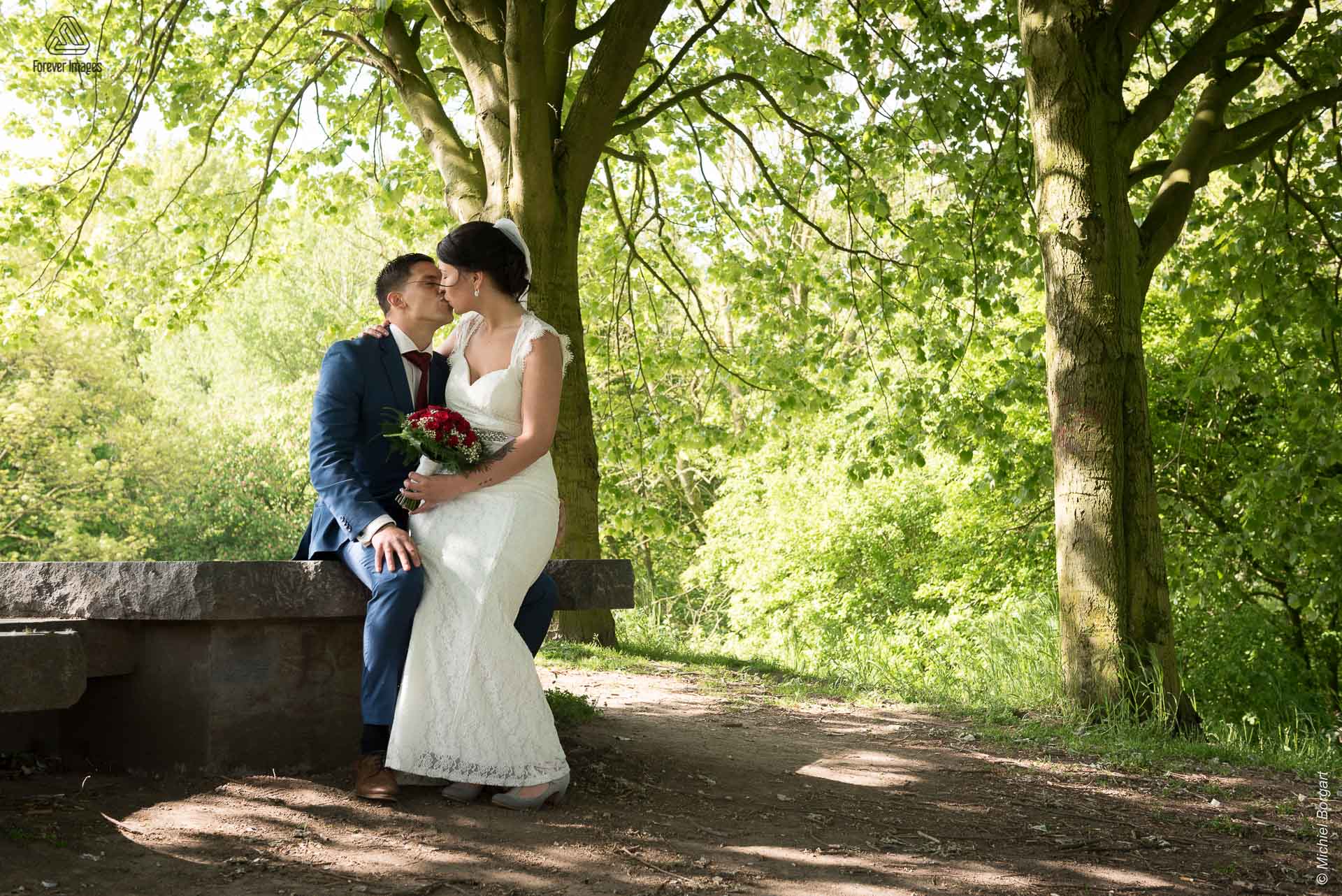 Bruidsfoto bruidspaar zittend kussend op heuvel in het park Oudegein in Nieuwegein | Kevin Leonie | Bruidsfotograaf Michiel Borgart - Forever Images.