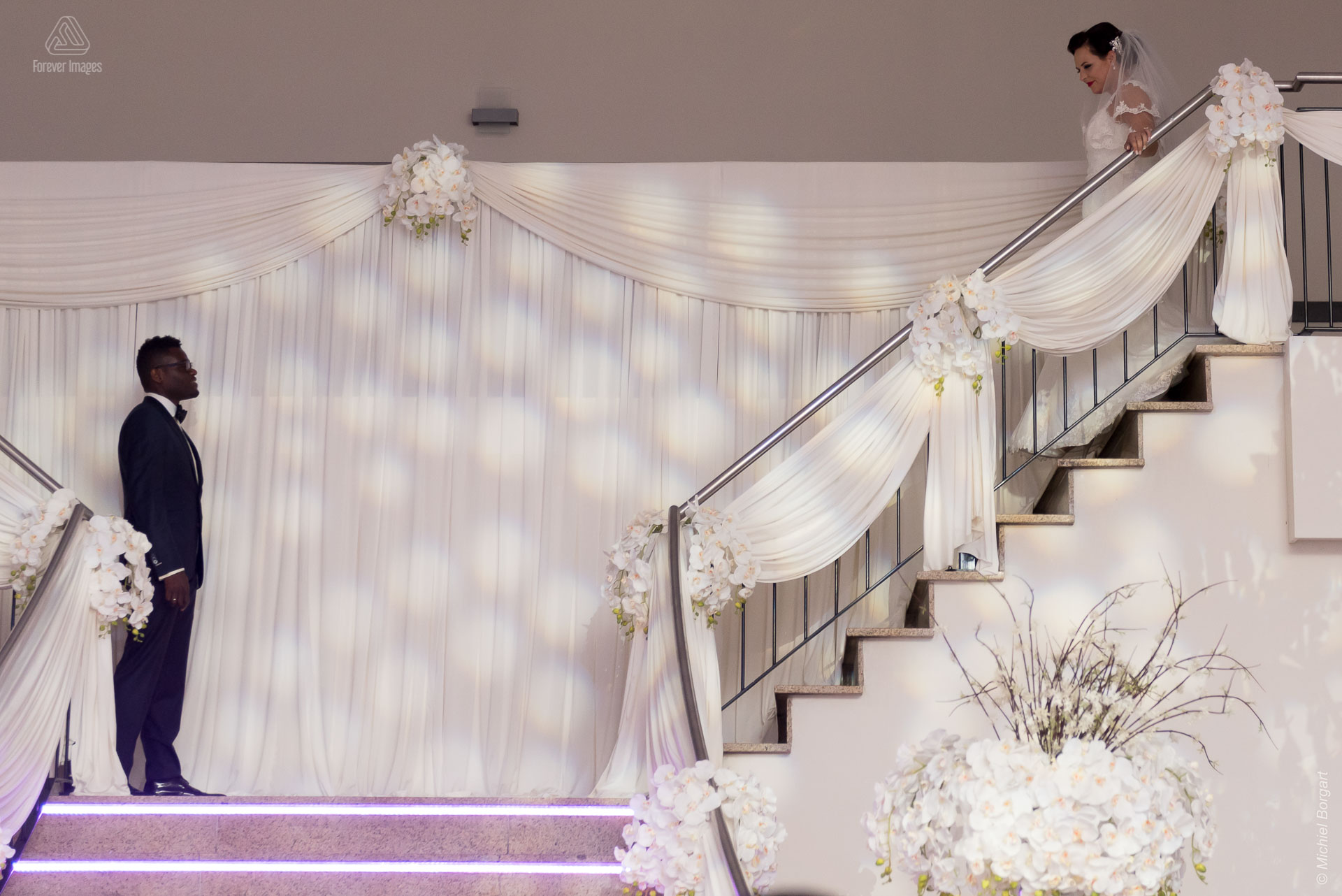 Bruidsfoto de bruidegom wacht beneden aan de trap op zijn bruid Amsterdam | Clarence Sabrina | Bruidsfotograaf Michiel Borgart - Forever Images.
