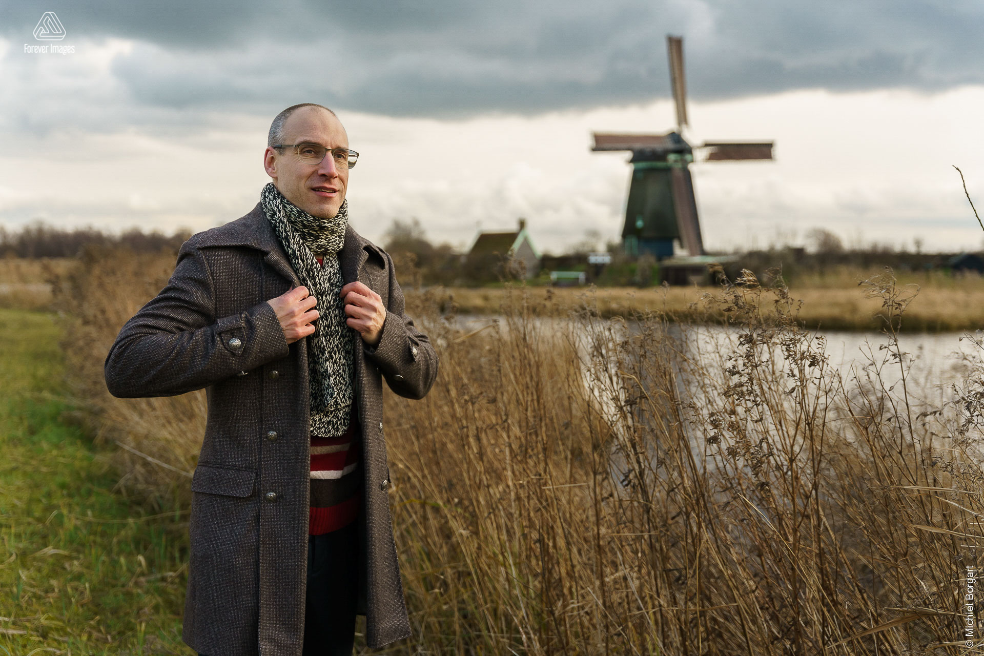Portrait photo man winter coat scarf at water and Dutch windmill | Robin Het Twiske De Stootersplas Twiskemolen | Portrait Photographer Michiel Borgart - Forever Images.