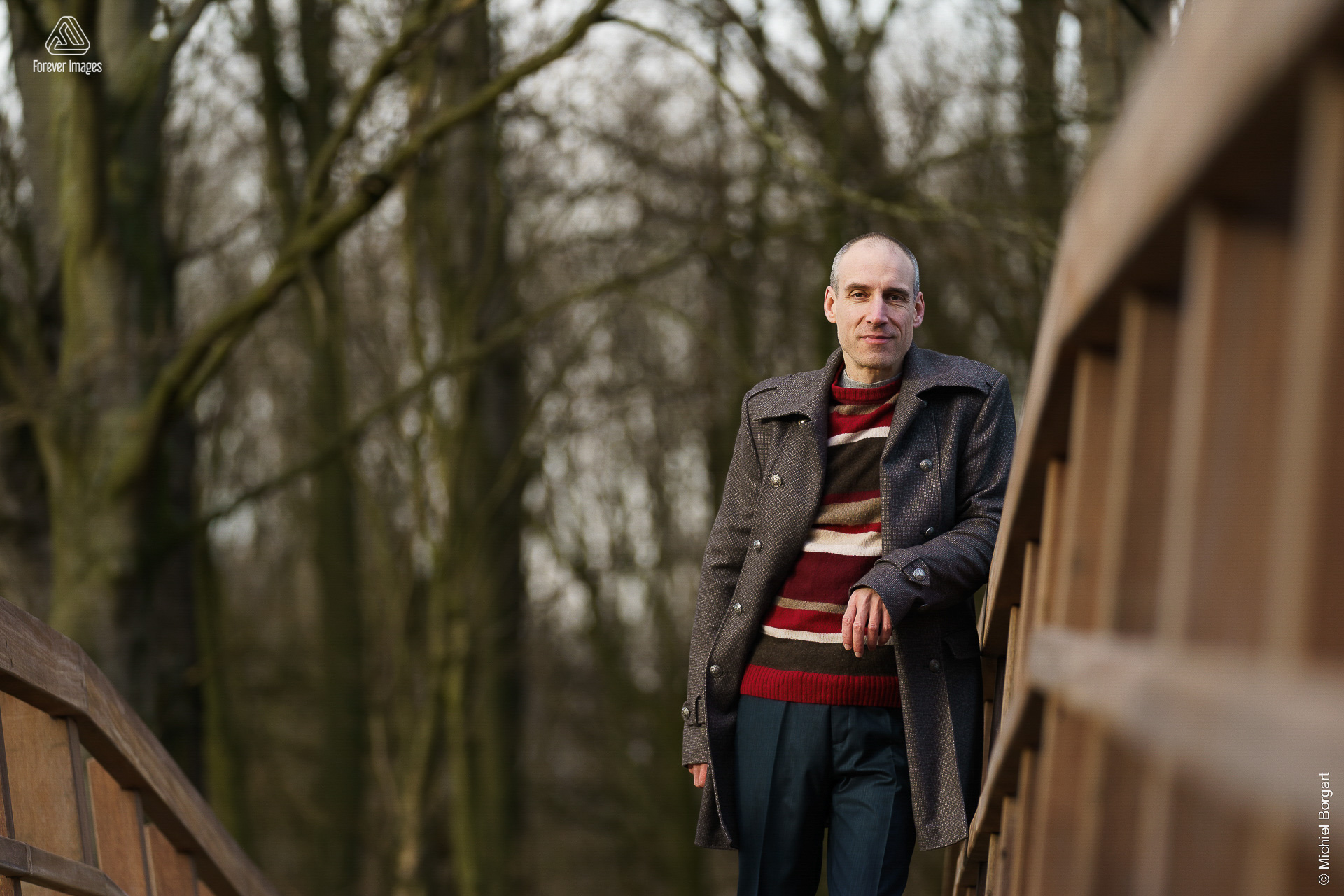 Portretfoto man op houten brug bij bos met glimlach | Robin Het Twiske De Stootersplas | Portretfotograaf Michiel Borgart - Forever Images.