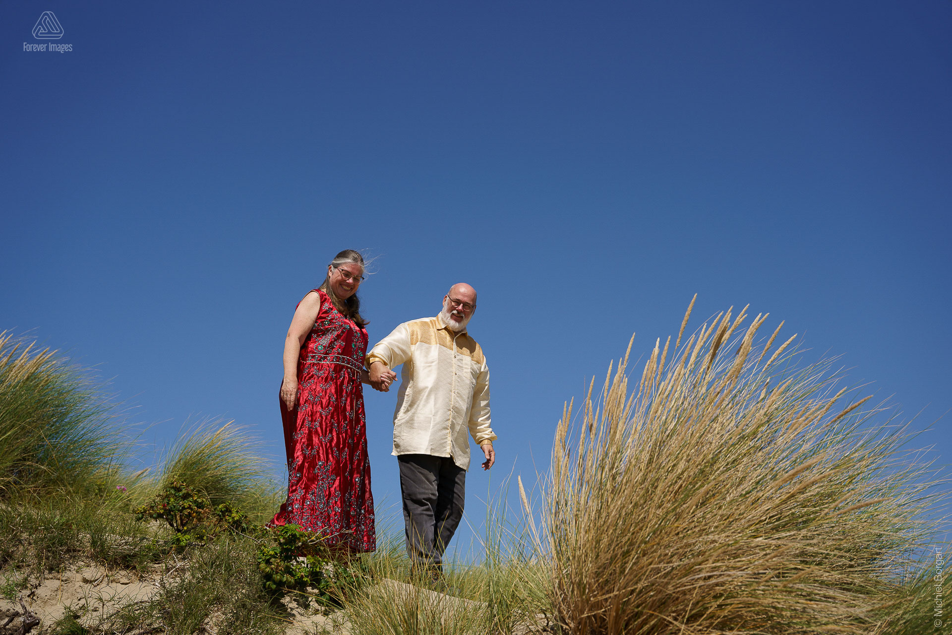 Portrait photo of a happy couple walking in the dunes with a clear blue sky | Henk | Portrait Photographer Michiel Borgart - Forever Images.