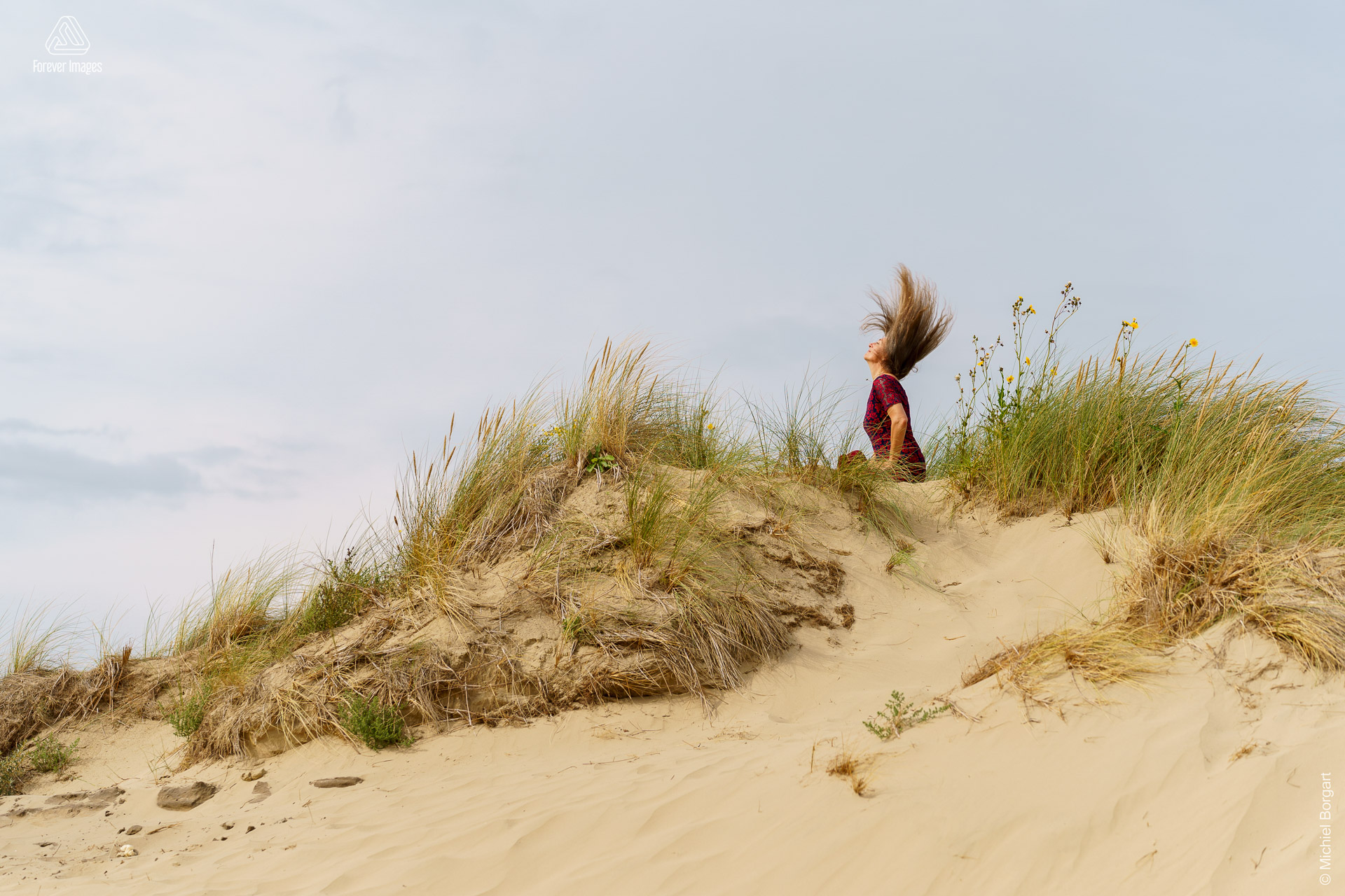 Portretfoto dame rode jurk hairflip in de duinen Kijkduin | Esther Echt Eigenwijs | Portretfotograaf Michiel Borgart - Forever Images.