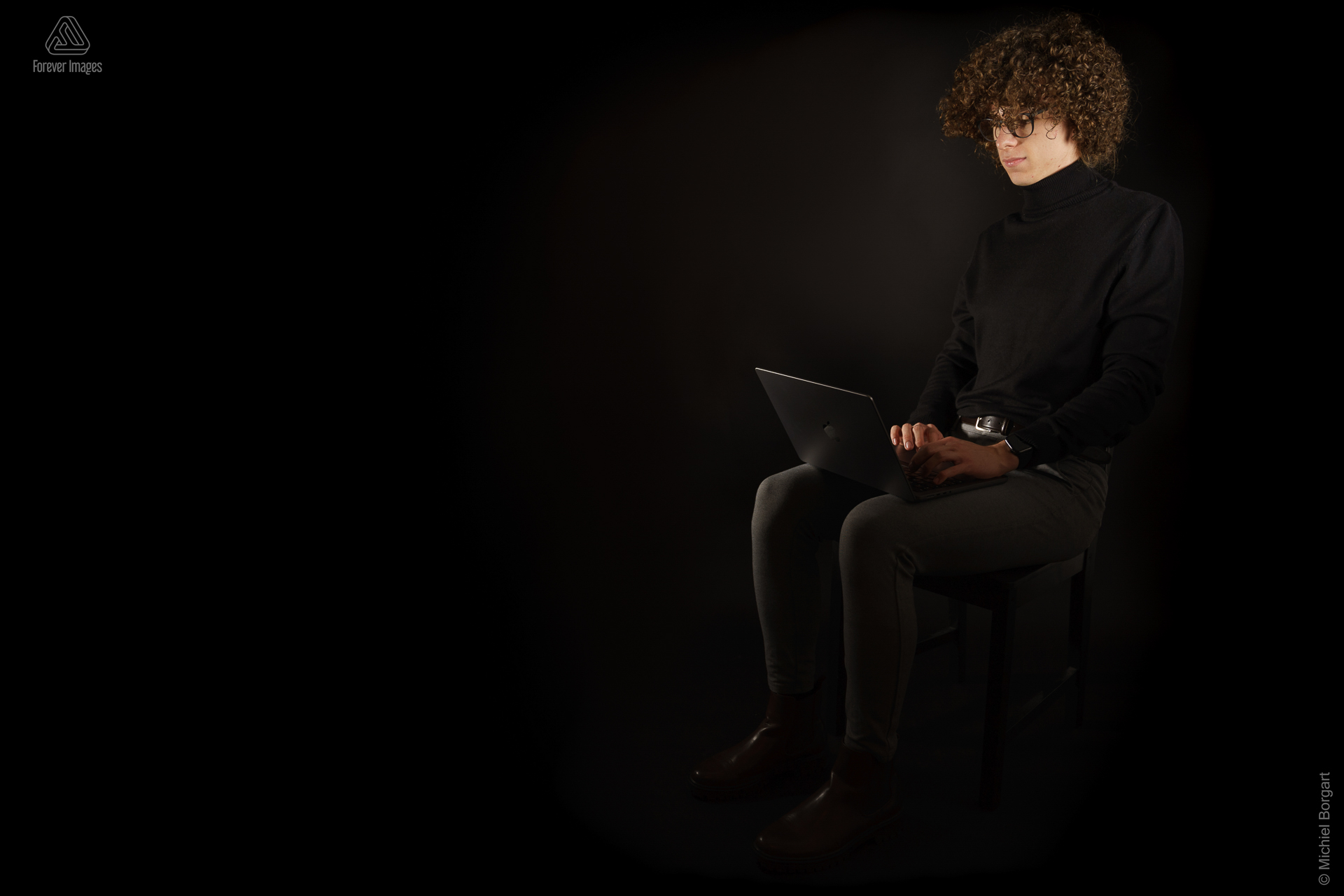 Portretfoto jonge man met zwarte coltrui lange krullende haren met laptop | Andreas | Portretfotograaf Michiel Borgart - Forever Images.