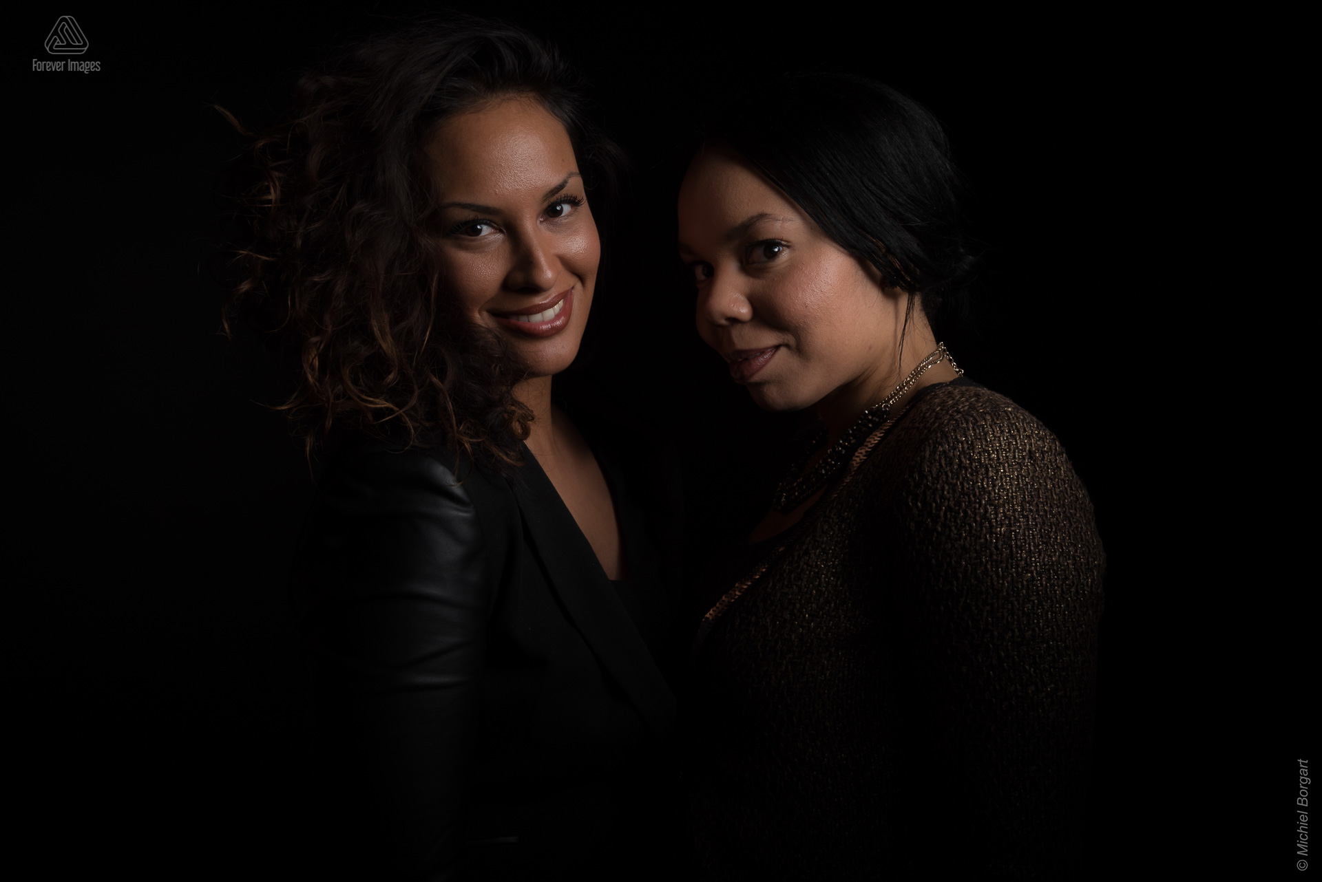 Portretfoto low-key film noir studio twee jonge dames lachend kijkend | Jessica Roos Jorgina Dalnoot | Portretfotograaf Michiel Borgart - Forever Images.