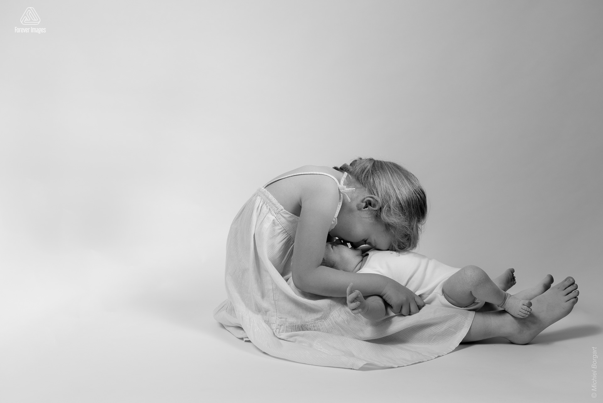 Portretfoto zwart-wit baby new born in de schoot van zijn beschermende grote zus | Rozelinde Kylian | Portretfotograaf Michiel Borgart - Forever Images.