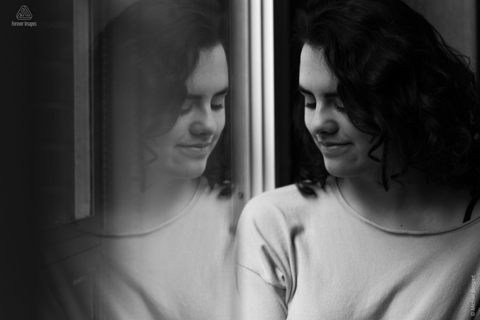 Portretfoto zwart-wit jonge dame kijkt naar beneden met reflectie in raam | Tessa Holscher | Portretfotograaf Michiel Borgart - Forever Images.