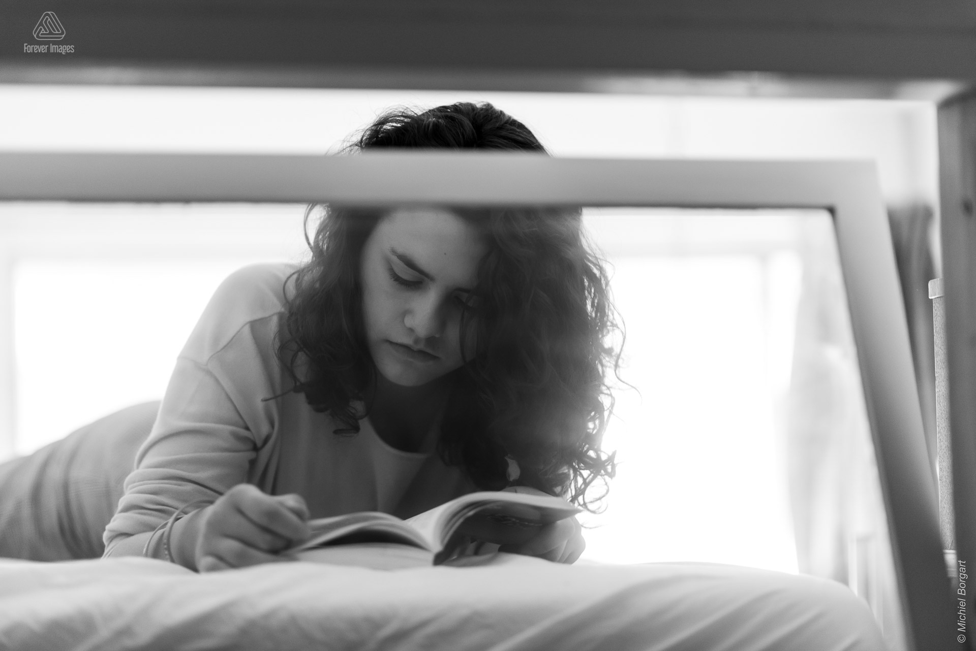 Portretfoto zwart-wit jonge dame leest boek op bed door raam | Tessa Holscher | Portretfotograaf Michiel Borgart - Forever Images.