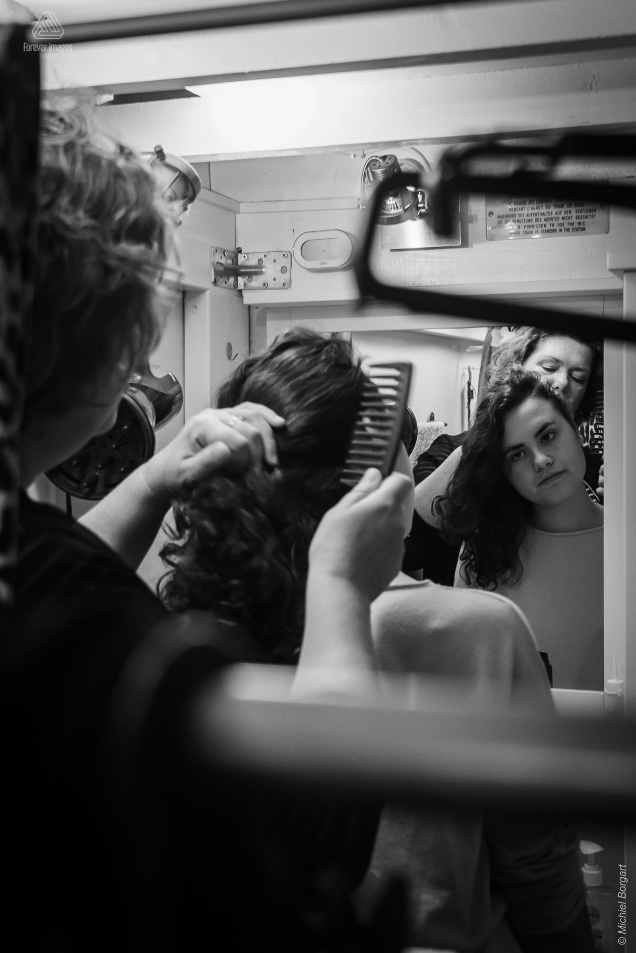 Portrait photo black and white B&W young lady hair beeing done looking in mirror | Tessa Holscher Betty Neijmeijer | Portrait Photographer Michiel Borgart - Forever Images.