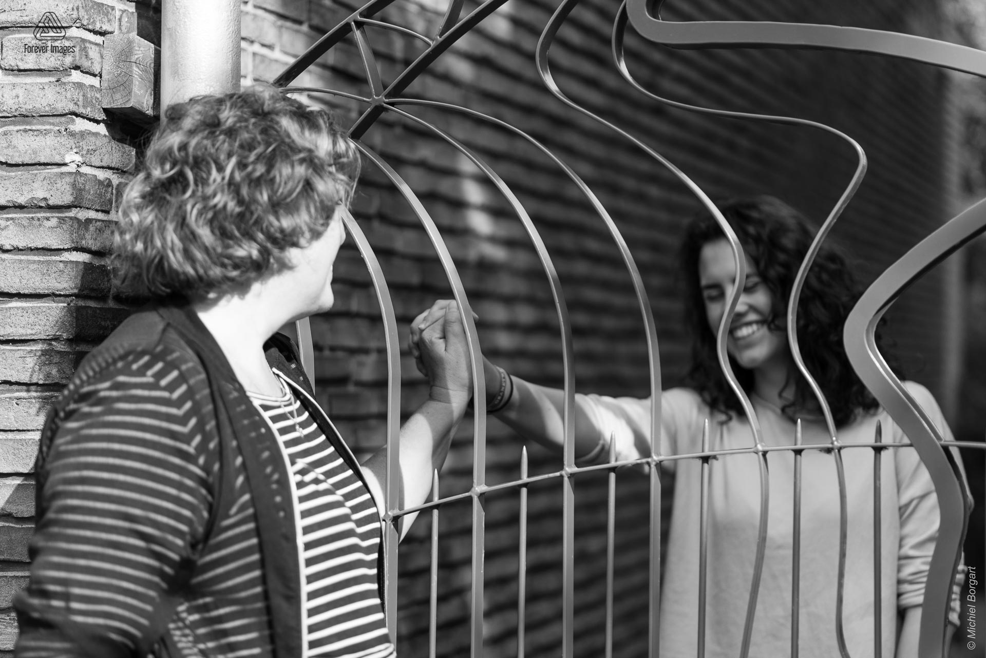 Portretfoto zwart-wit jonge dame achter hek houd hand vast van moeder | Tessa Holscher Betty Neijmeijer | Portretfotograaf Michiel Borgart - Forever Images.