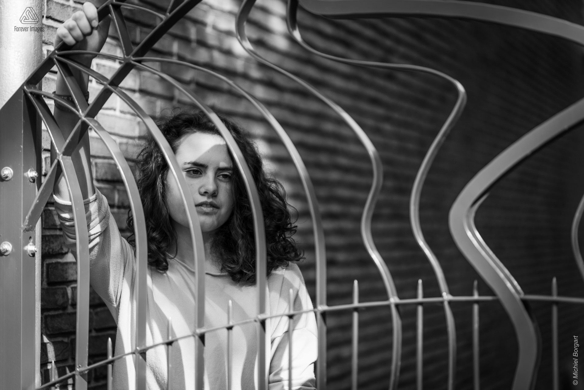 Portretfoto zwart-wit jonge dame houd hek vast en kijkt opzij | Tessa Holscher | Portretfotograaf Michiel Borgart - Forever Images.
