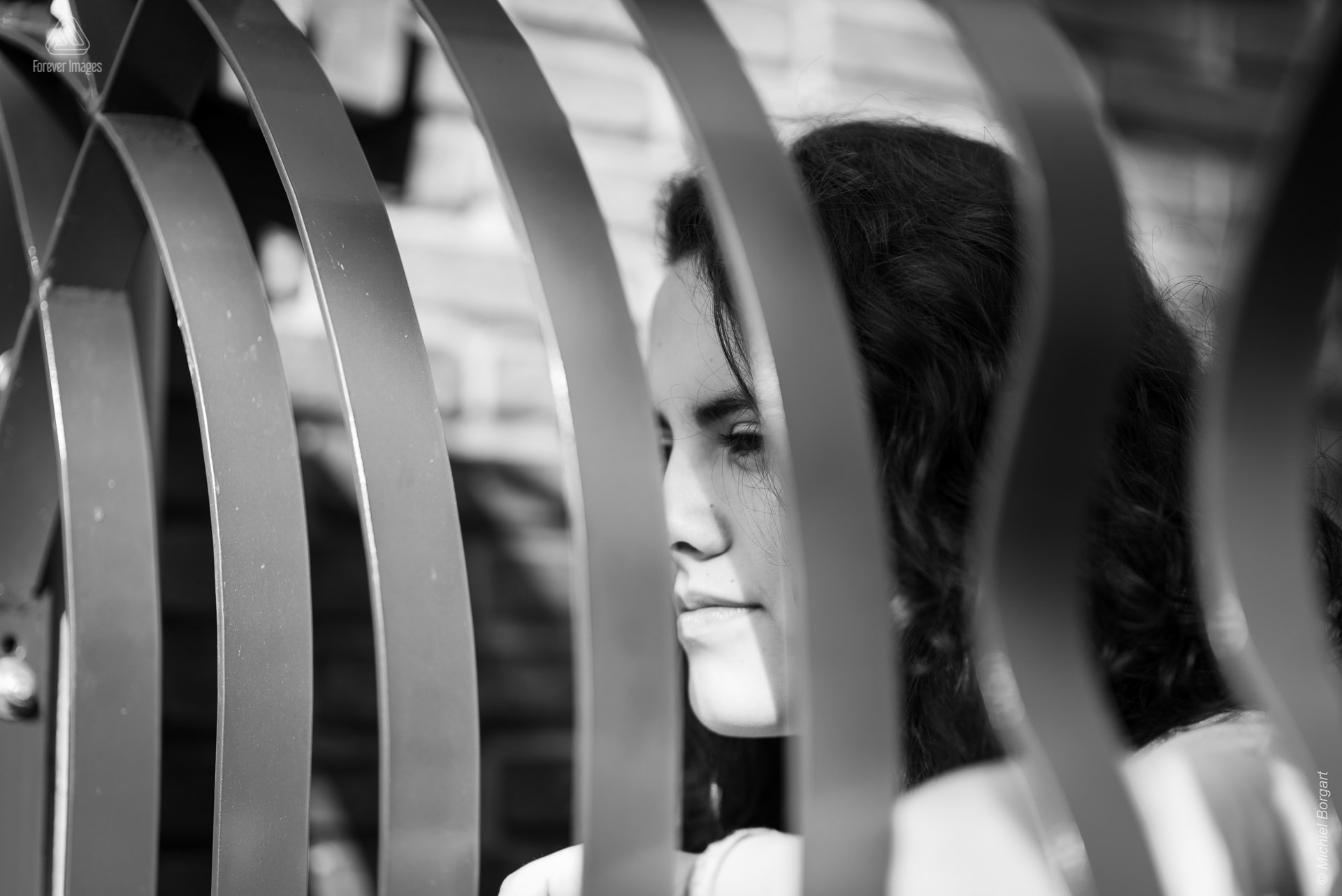 Portretfoto zwart-wit jonge dame kijkt door hek | Tessa Holscher | Portretfotograaf Michiel Borgart - Forever Images.