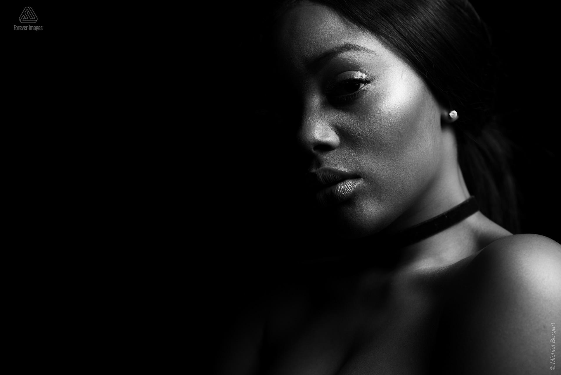 Portretfoto zwart-wit glamourshoot chocker kijkend in camera low key | Mariana Pietersz Natasha Mondesir | Portretfotograaf Michiel Borgart - Forever Images.