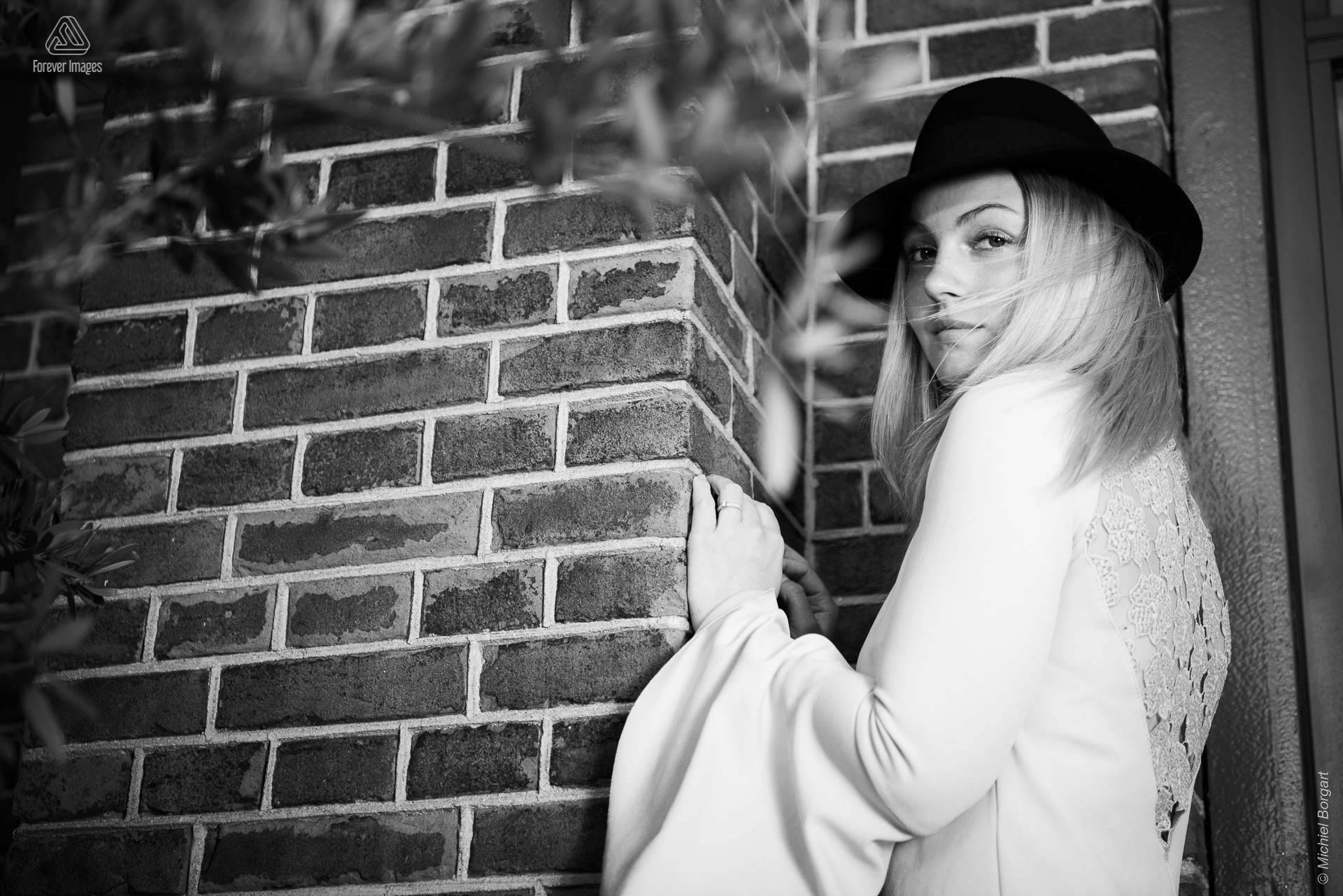 Portrait photo black and white young lady sheltered in the wind with black hat | Porscha Luna de Jong Happyhappyjoyjoy | Portrait Photographer Michiel Borgart - Forever Images.