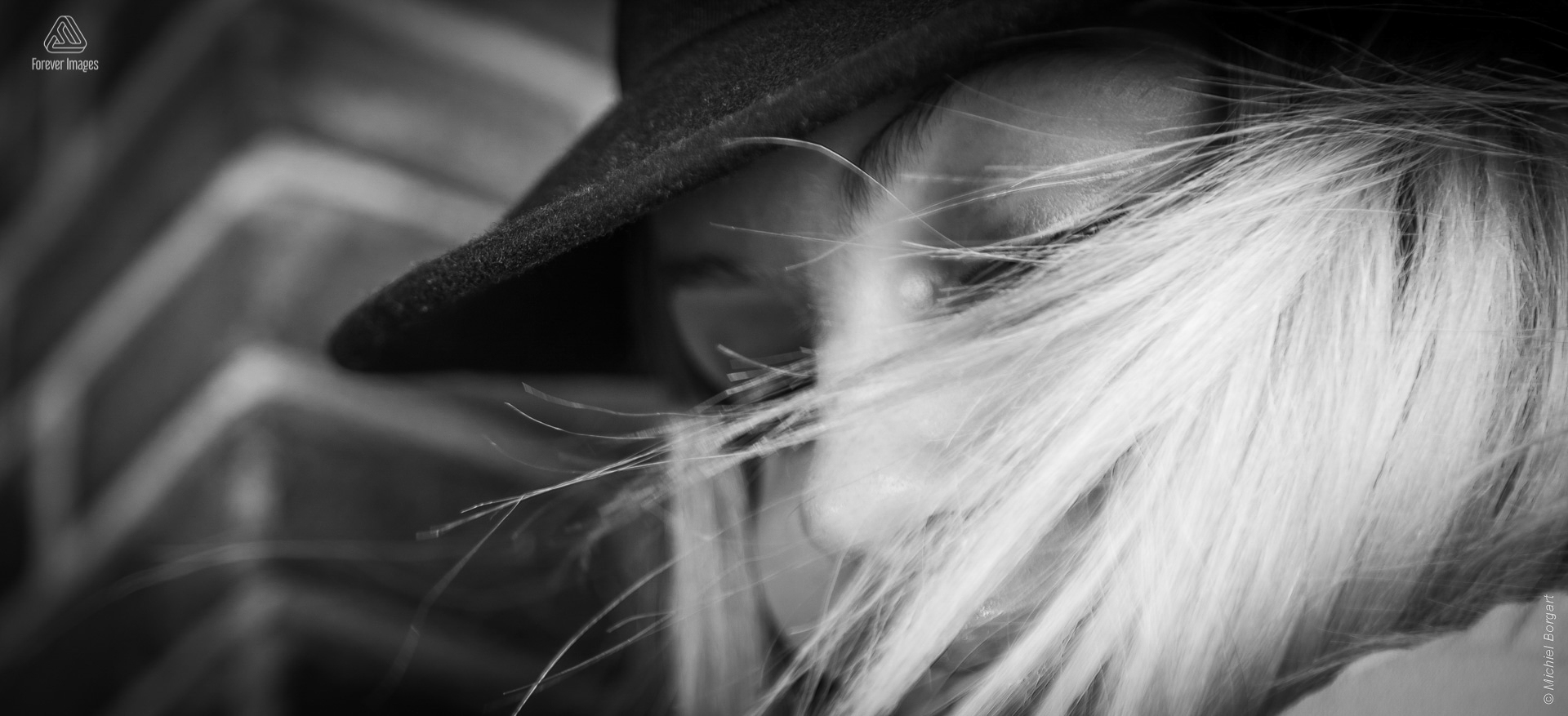 Portretfoto zwart-wit jonge dame hoed verscholen achter blonde haren | Porscha Luna de Jong Happyhappyjoyjoy | Portretfotograaf Michiel Borgart - Forever Images.