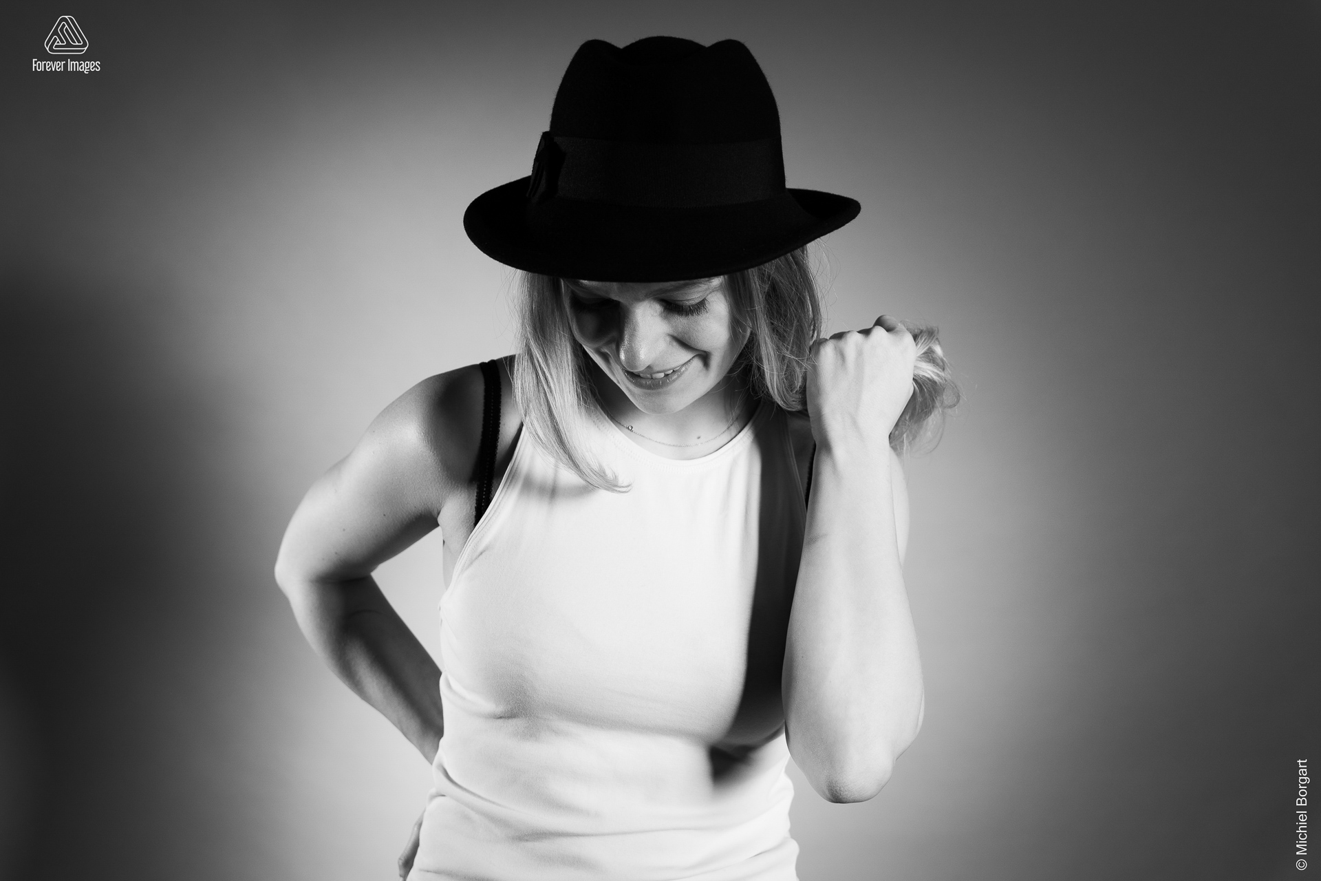 Portretfoto zwart-wit jonge dame wit hemdje zwarte hoed hand door haar | Fanziska | Portretfotograaf Michiel Borgart - Forever Images.
