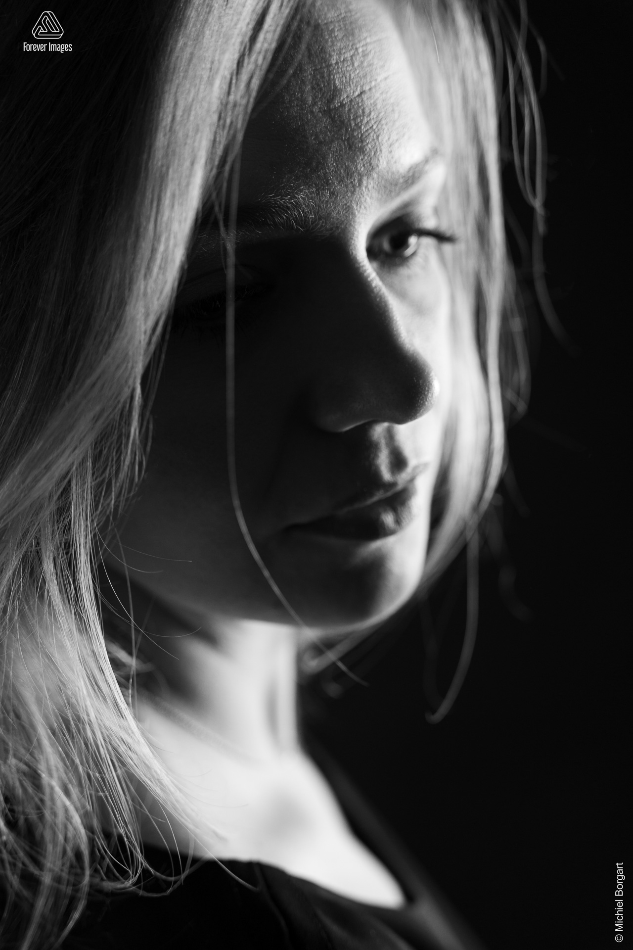 Portretfoto zwart-wit low key jonge dame met zwart jurkje kijkend opzij | Fanziska | Portretfotograaf Michiel Borgart - Forever Images.