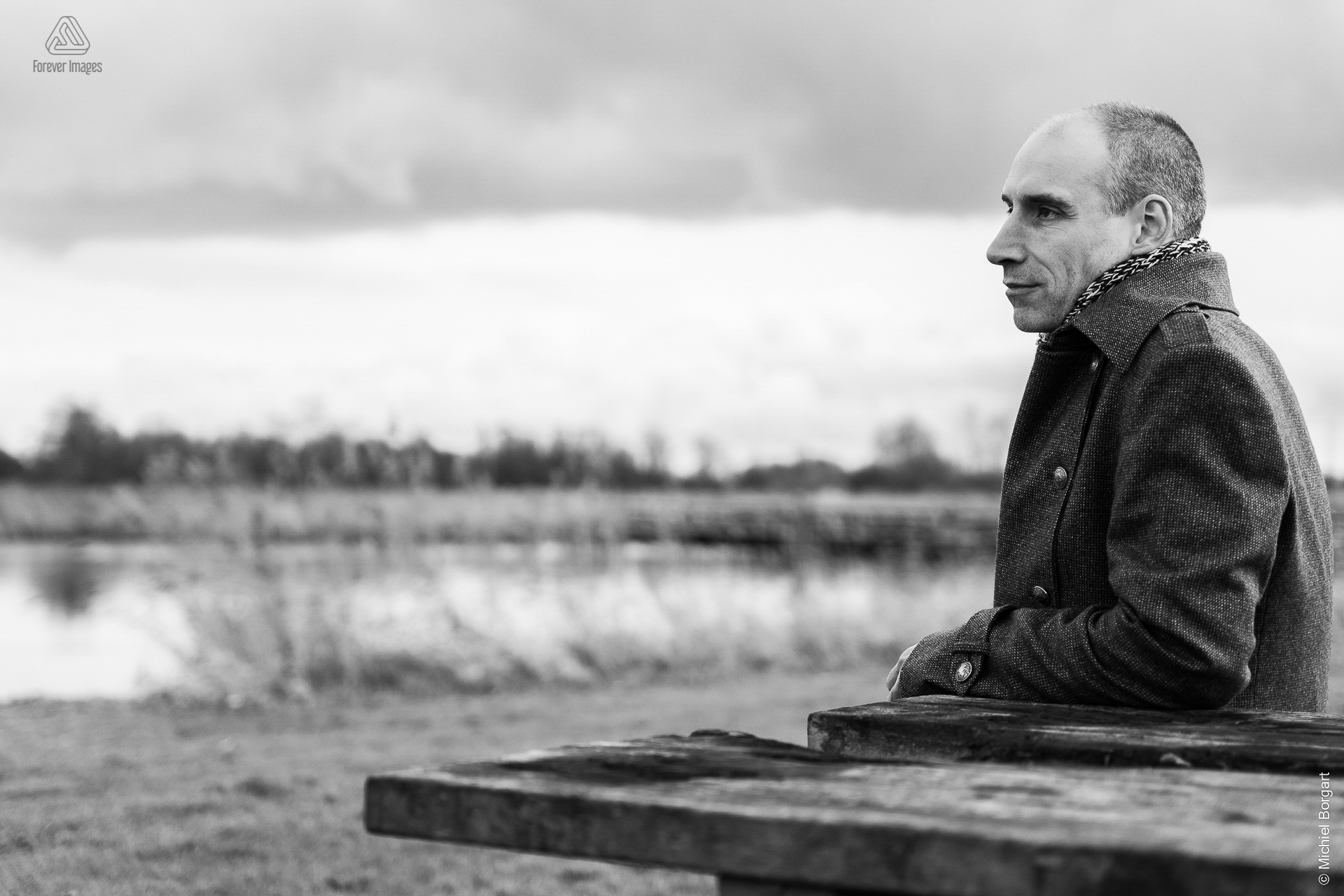 Portrait photo black and white B&W man sitting at wooden table by water | Robin Het Twiske De Stootersplas | Portrait Photographer Michiel Borgart - Forever Images.