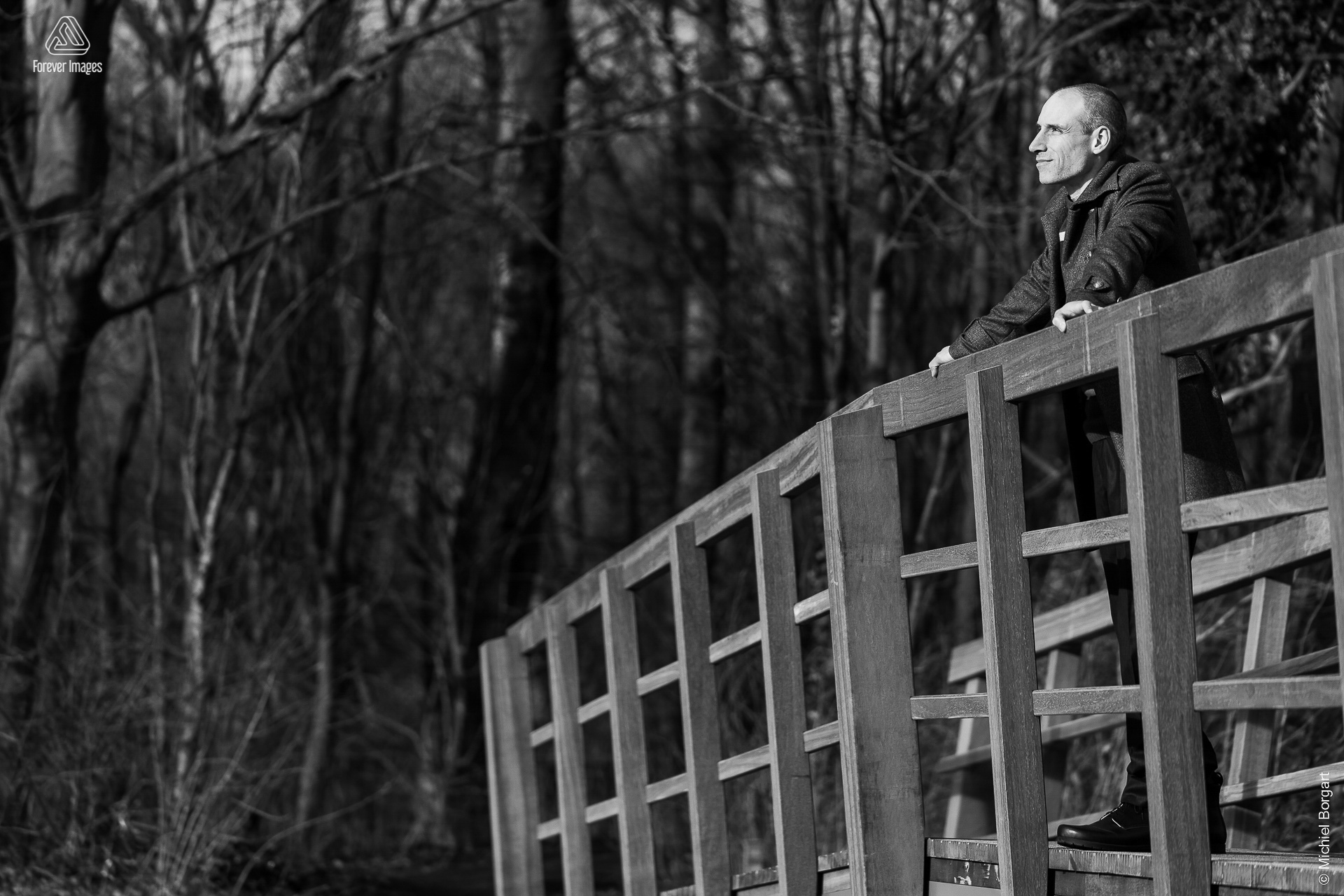 Portrait photo black and white B&W man on wooden bridge looking forward smile | Robin Het Twiske De Stootersplas | Portrait Photographer Michiel Borgart - Forever Images.
