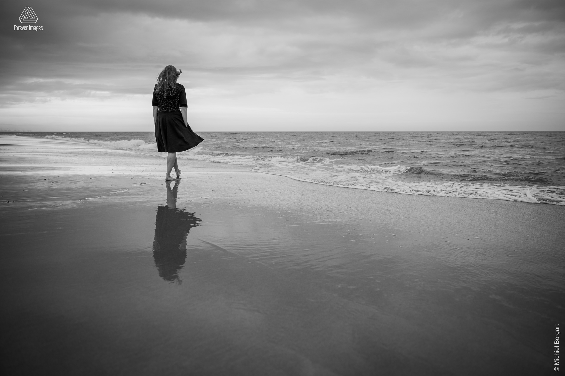 Portretfoto zwart-wit dame wandelt op het strand Kijkduin | Esther Echt Eigenwijs | Portretfotograaf Michiel Borgart - Forever Images.
