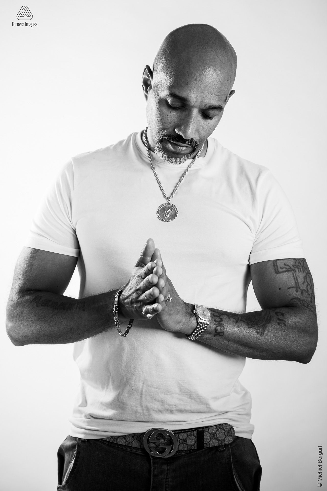 Portretfoto zwart-wit man met tattoo in wit t-shirt handen tegen elkaar | Marchall Breidel | Portretfotograaf Michiel Borgart - Forever Images.