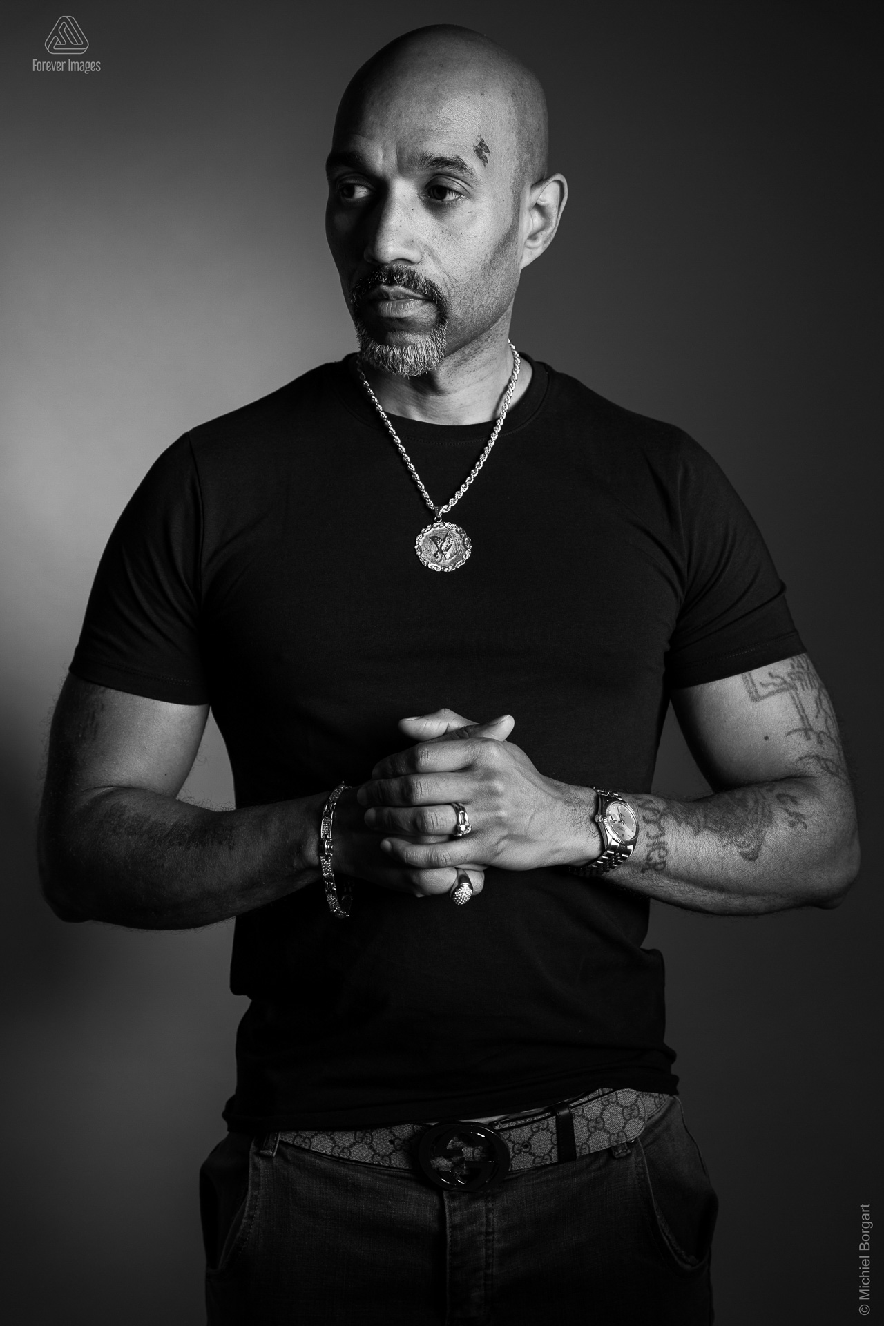 Portretfoto zwart-wit man met tattoo in zwart t-shirt handen ineengeslagen | Marchall Breidel | Portretfotograaf Michiel Borgart - Forever Images.