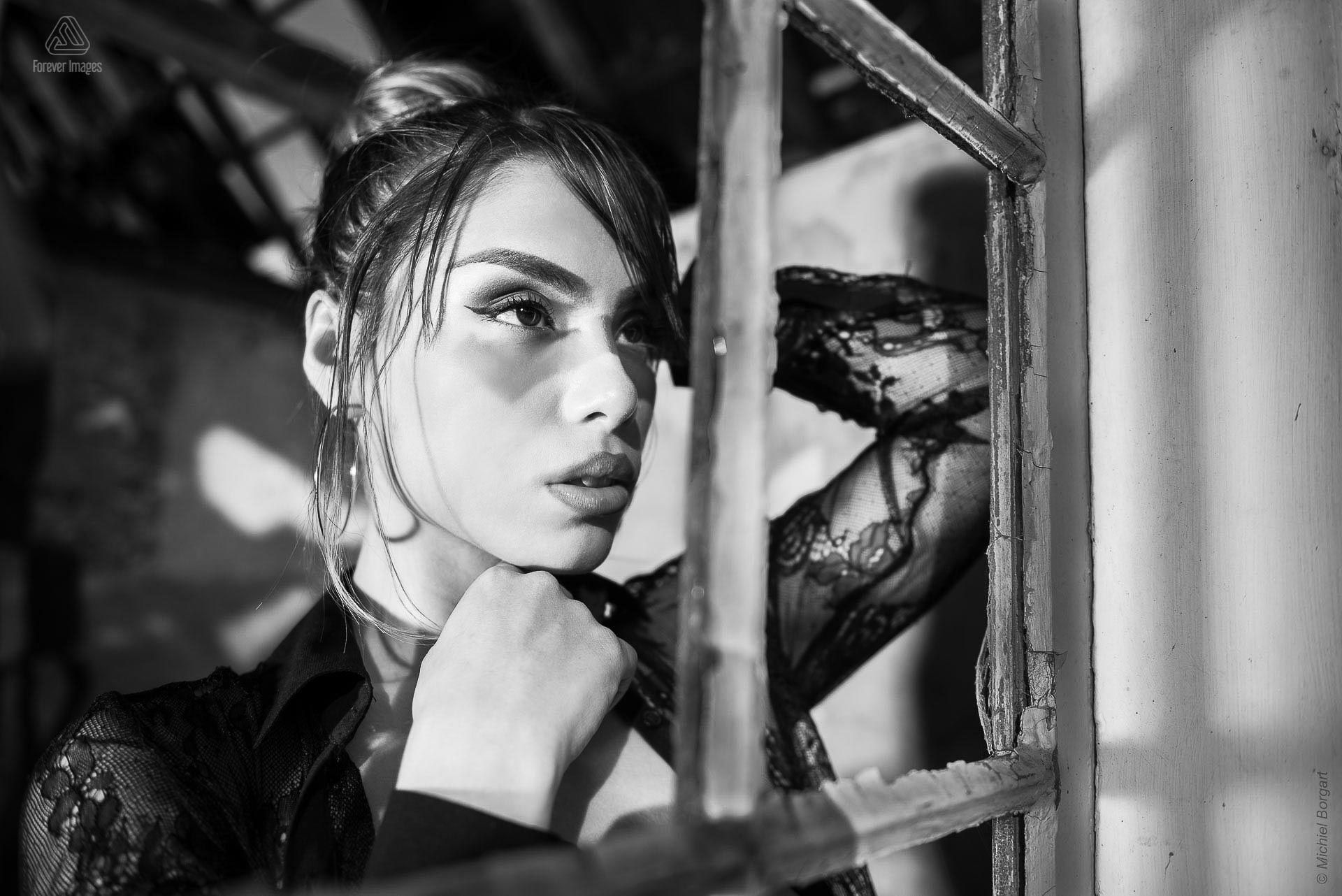 Portretfoto urbex zwart-wit mooie dame kijkt door gebroken raam | Floriana Horta | Portretfotograaf Michiel Borgart - Forever Images.